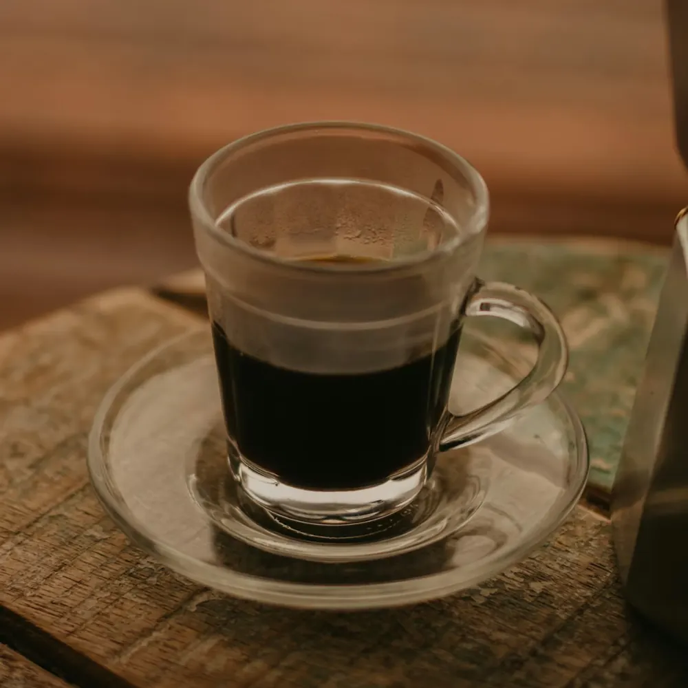Glass cup of black coffee on a saucer on a rustic wooden table
